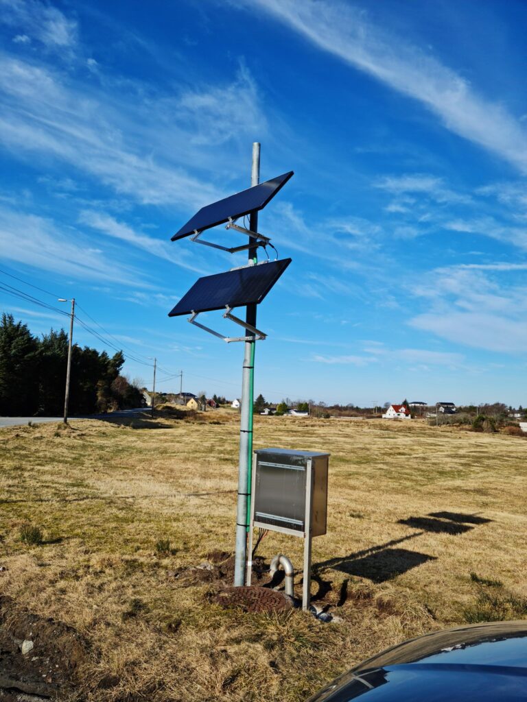 Solar panels mounted on a pole in a grassy field with a clear blue sky in the background.