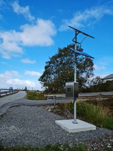 En modern elektronisk vägtullupptagningsutrustning belägen bredvid en väg under en klarblå himmel med få moln.