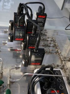 Flera alicat massflödesregulatorer anslutna till ett system av metallrör och ventiler, arrangerade på en laboratoriebänk.