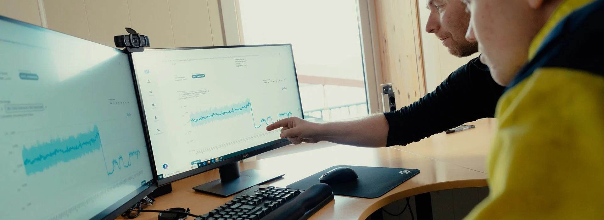 Two men analyzing data on a dual monitor computer in a bright office.